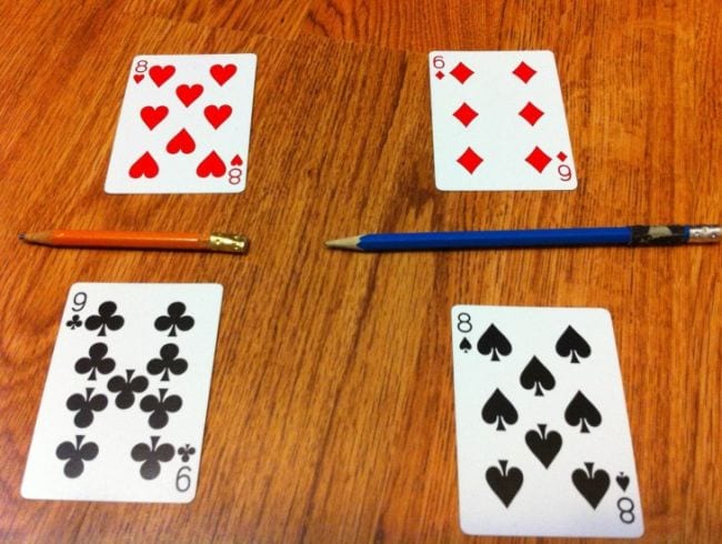 Four playing cards laid out to represent fractions with pencils for lines
