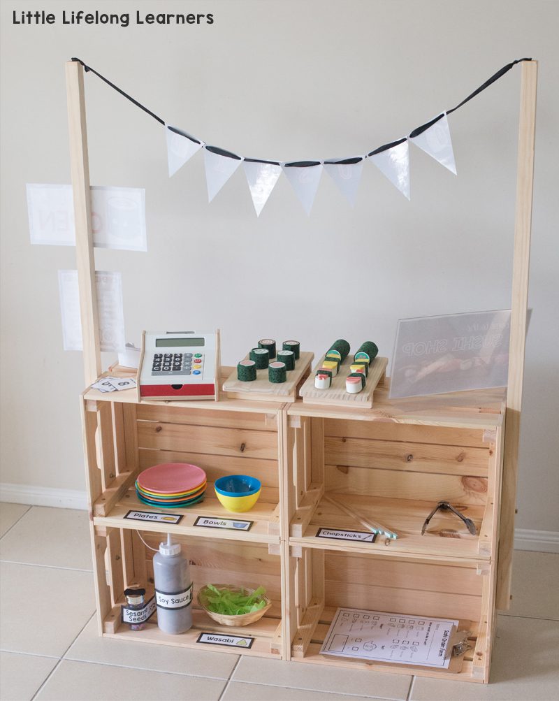 Four wooden crates are assembled to form a toy farm stand. A cash register and some fake food are included.